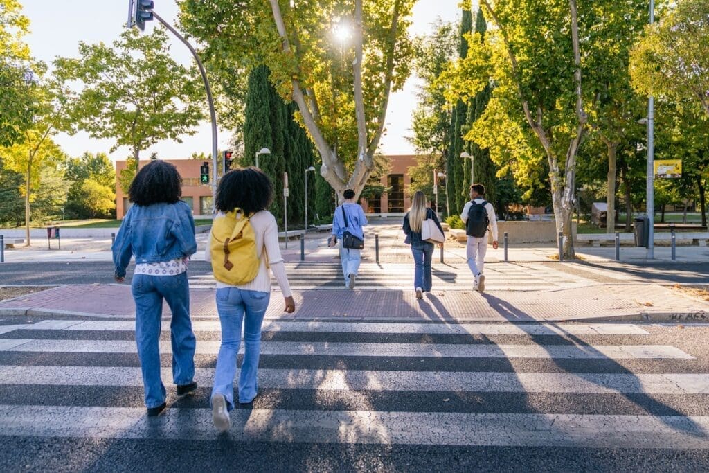 Multiracial students walking on a zebra crossing outside a university campus, showing diversity and education concept